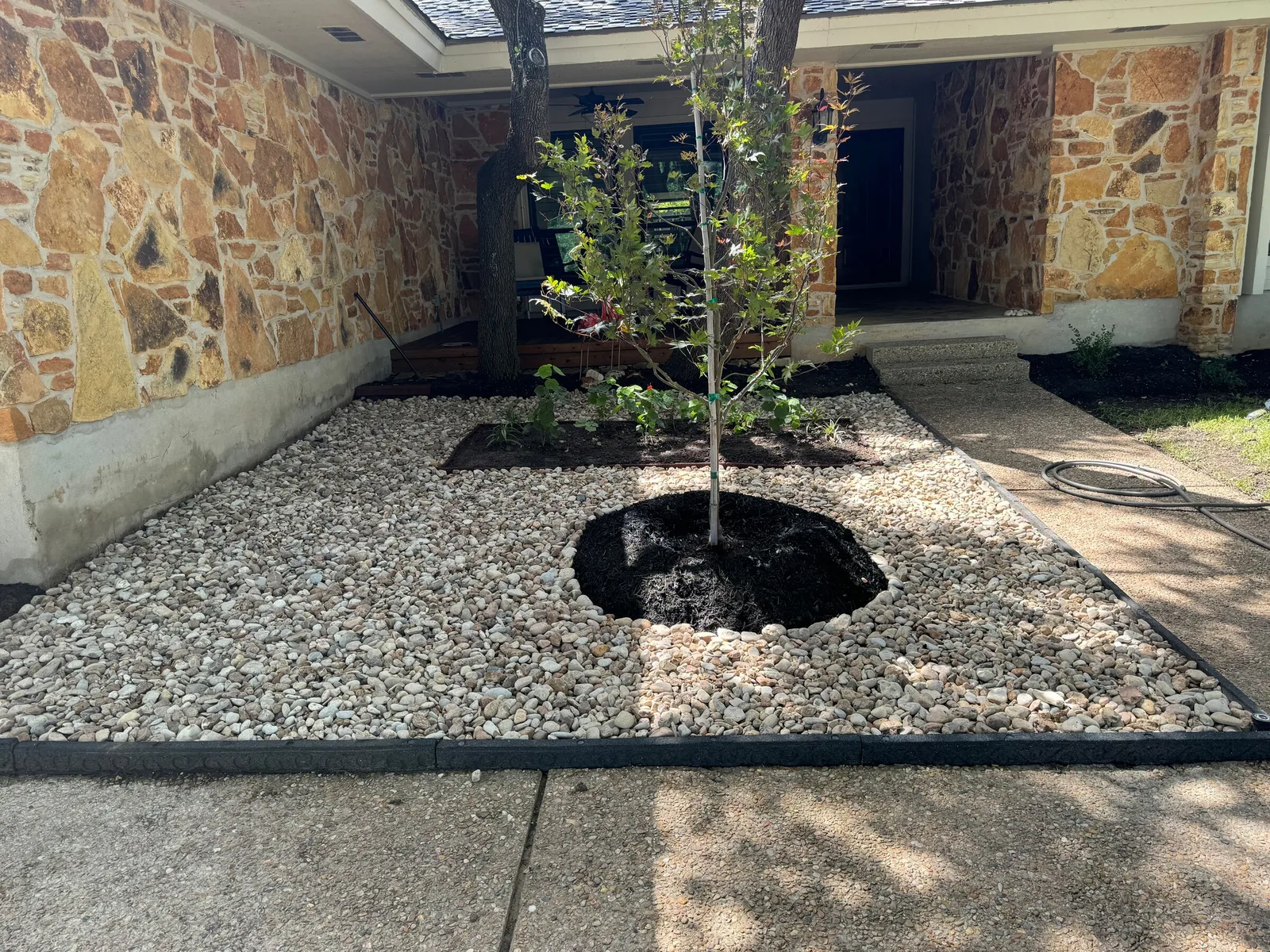 The same entry planting bed filled with light decorative rock around the small tree.