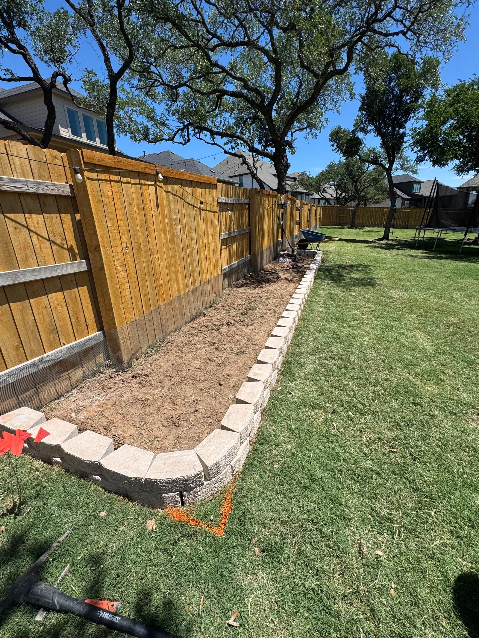 A long planting bed with stone edging along a wood privacy fence and lawn.