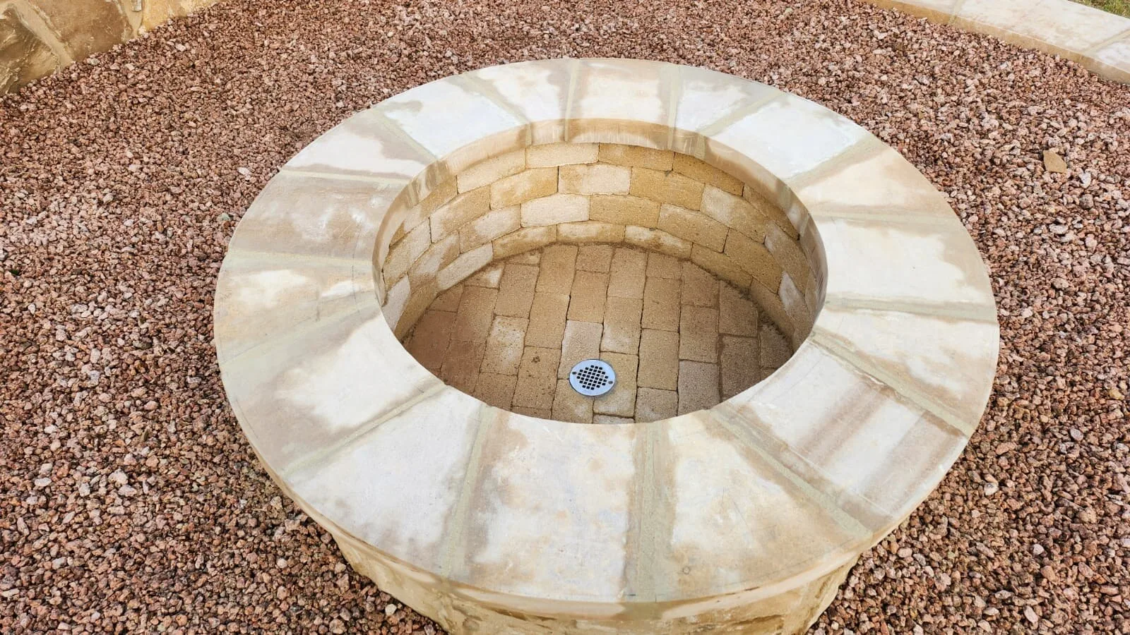A close view of a round limestone fire pit set in red gravel.