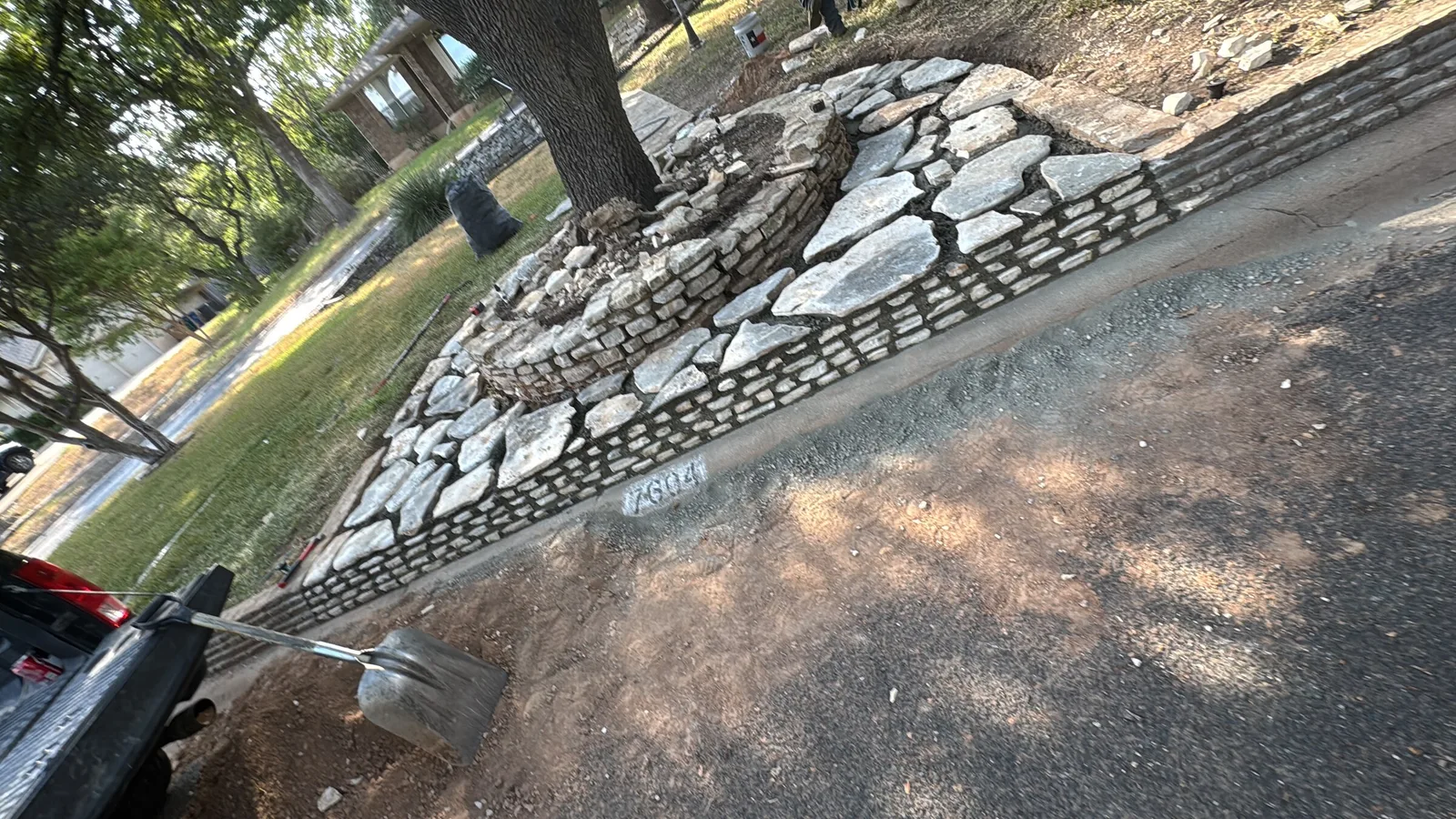 Flagstone and a low stacked-stone border curving between a lawn and a driveway.