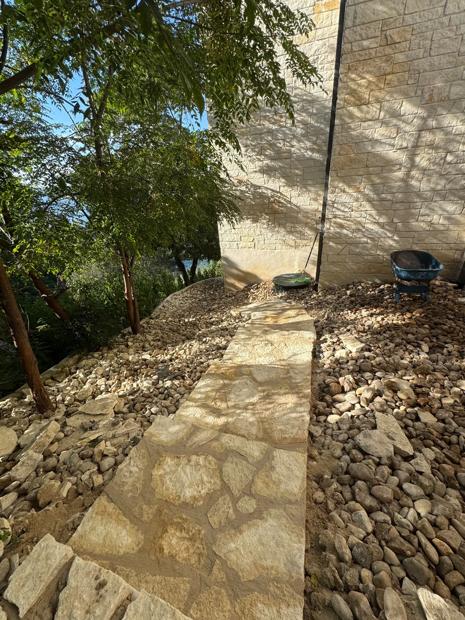A tan flagstone path running between river rock beds beside a limestone house.