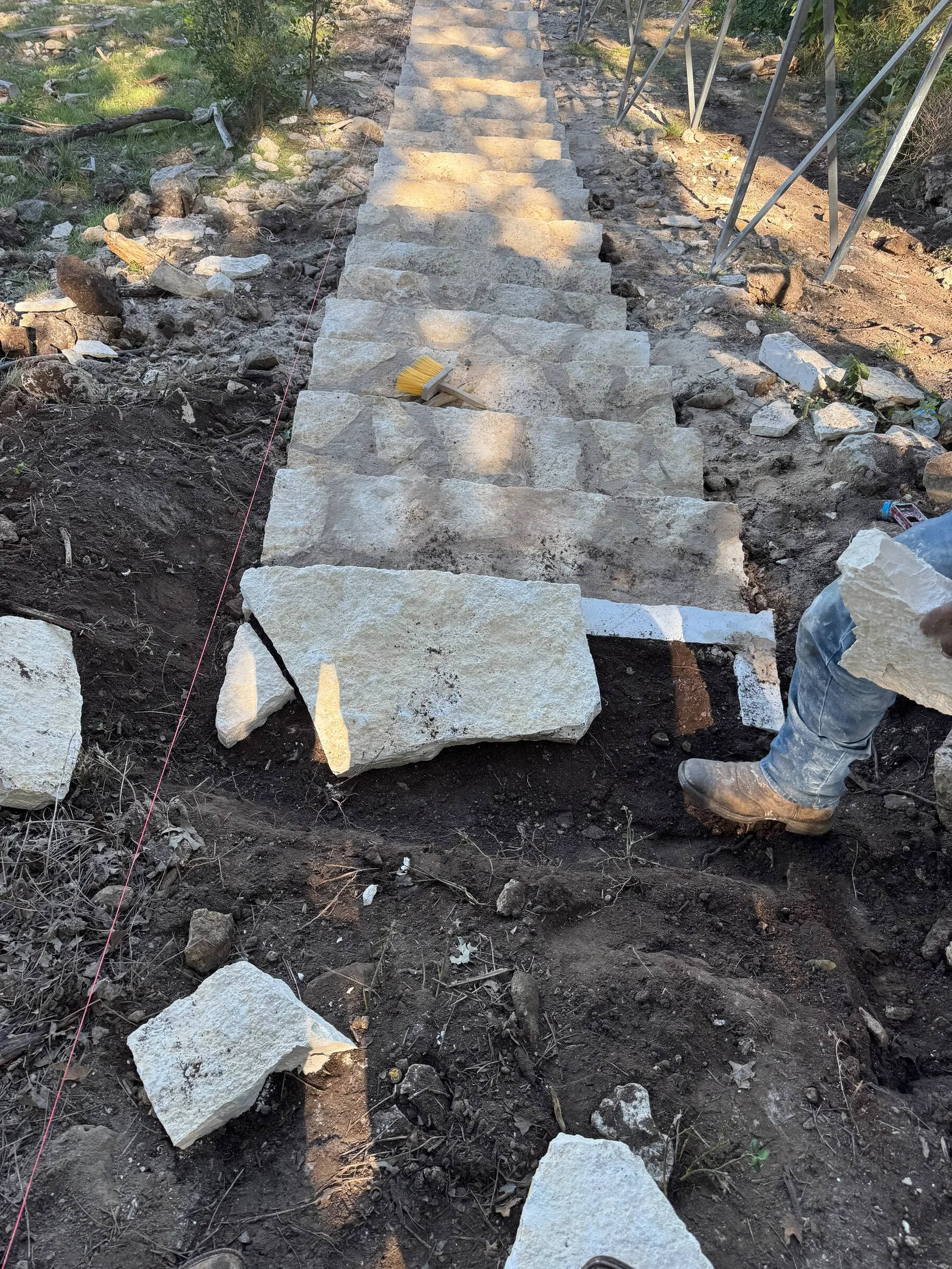 Pale flagstone pieces being set as steps up a slope of loose soil.