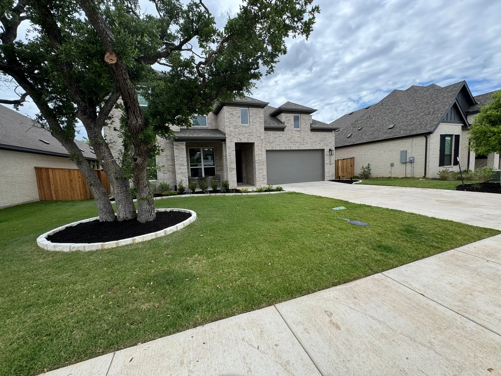 A large oak in a front lawn circled by a white stone ring and dark mulch.