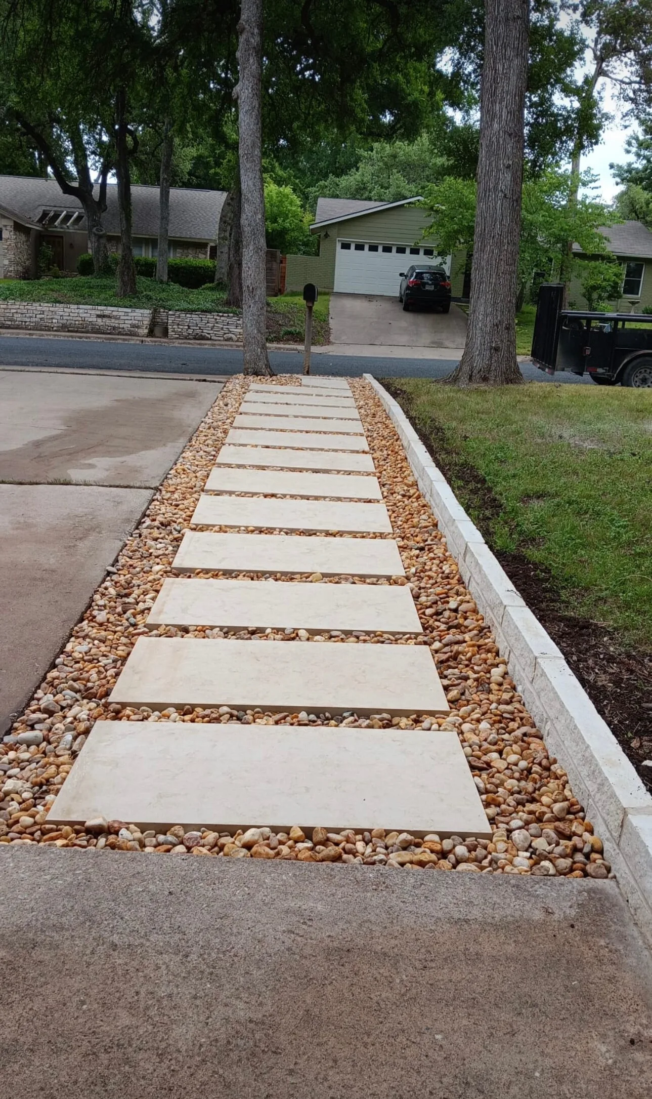 Rectangular pavers set in decorative gravel beside a driveway.