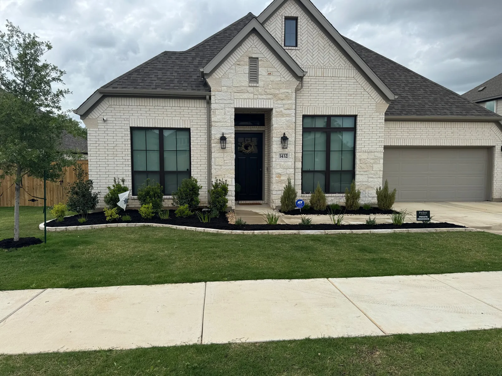 A limestone home with planted front beds, a curved white border and a green lawn.