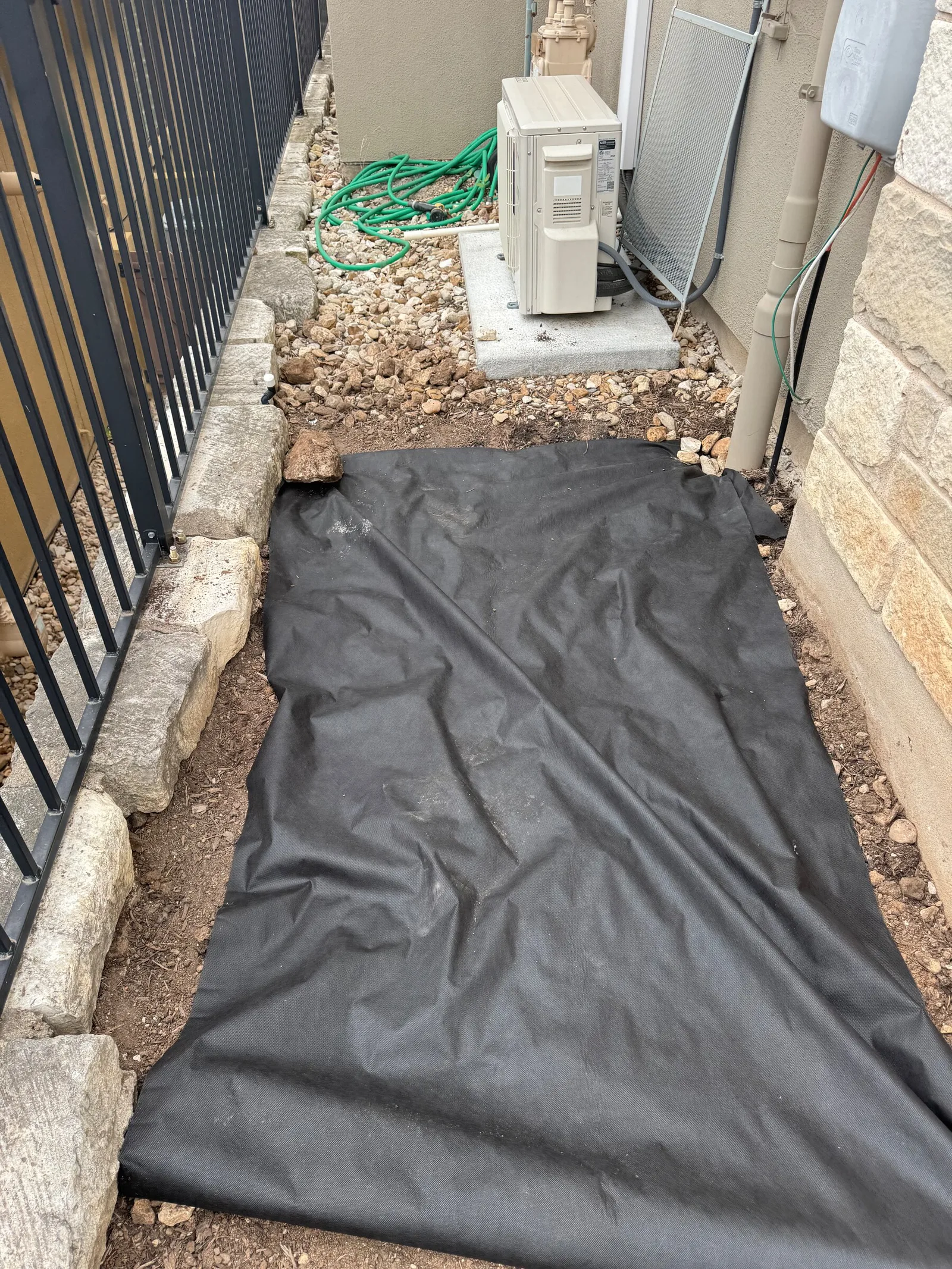 Black landscape fabric laid between stone edging in a narrow side yard.