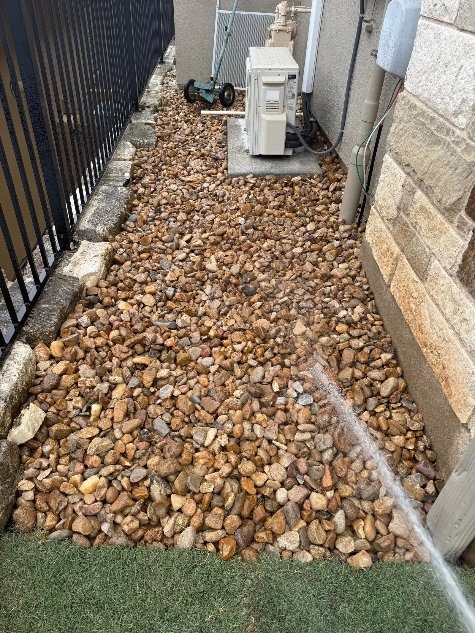 Brown river rock covering the same narrow side yard between stone edging.
