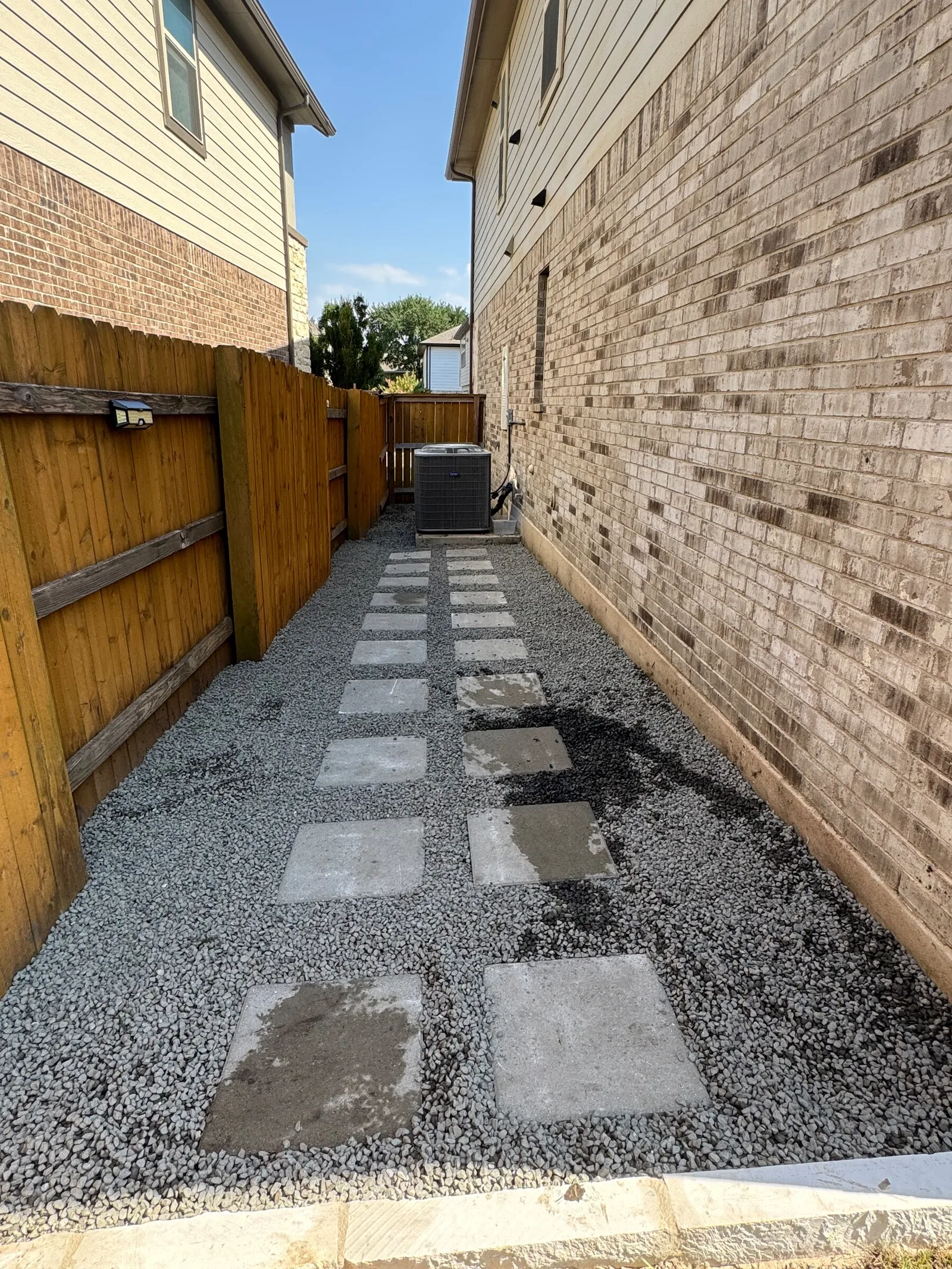 Gray gravel with square stepping pavers along the same fenced side yard.
