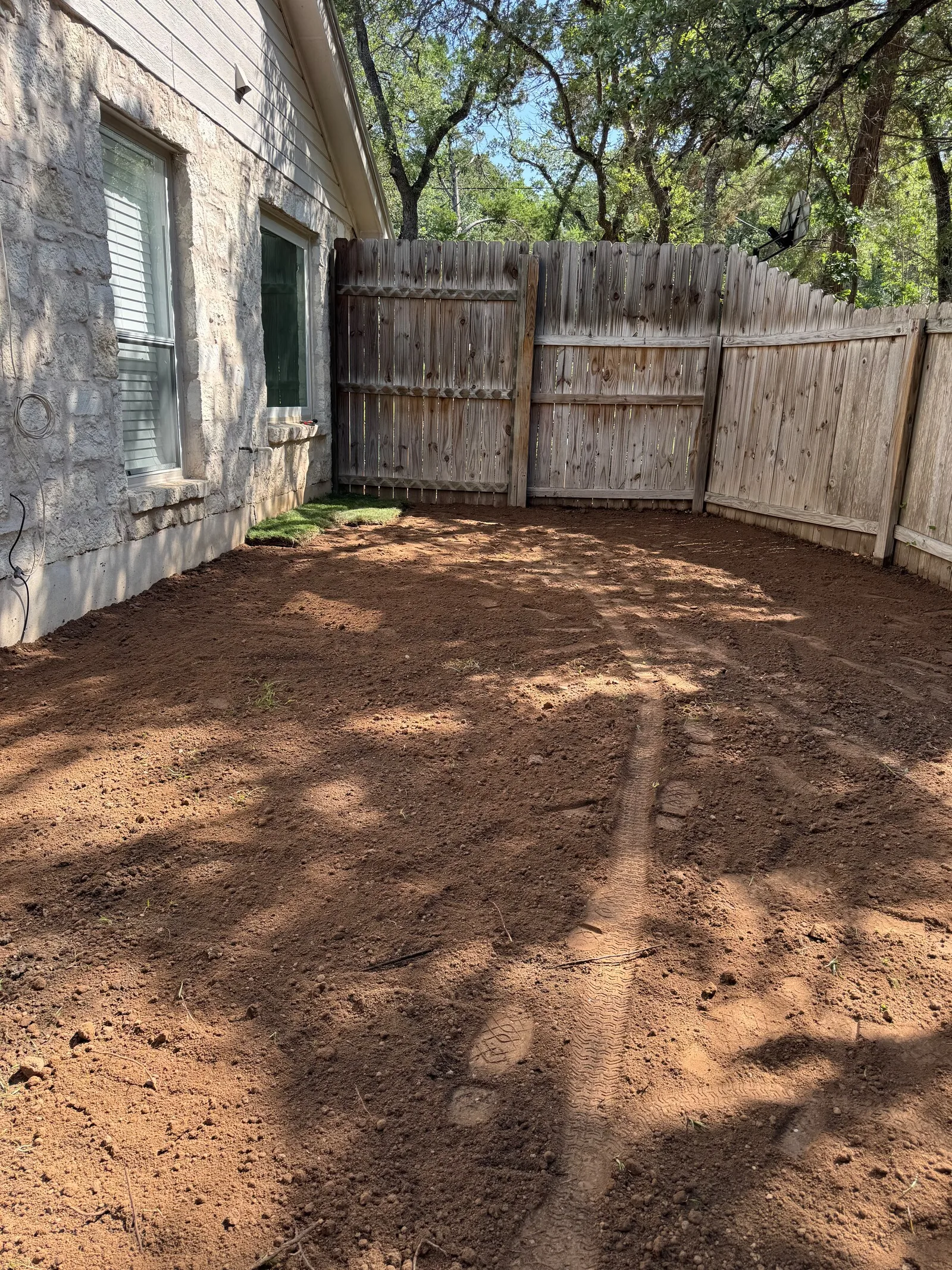 Bare graded soil in a fenced side yard beside a stone house.