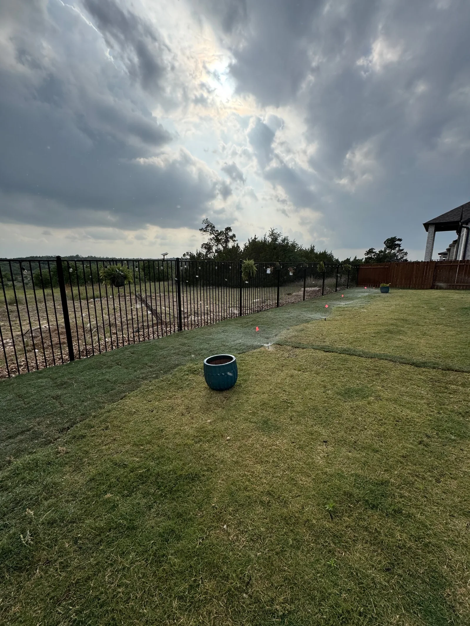 A full green lawn along an iron fence under a cloudy sky.