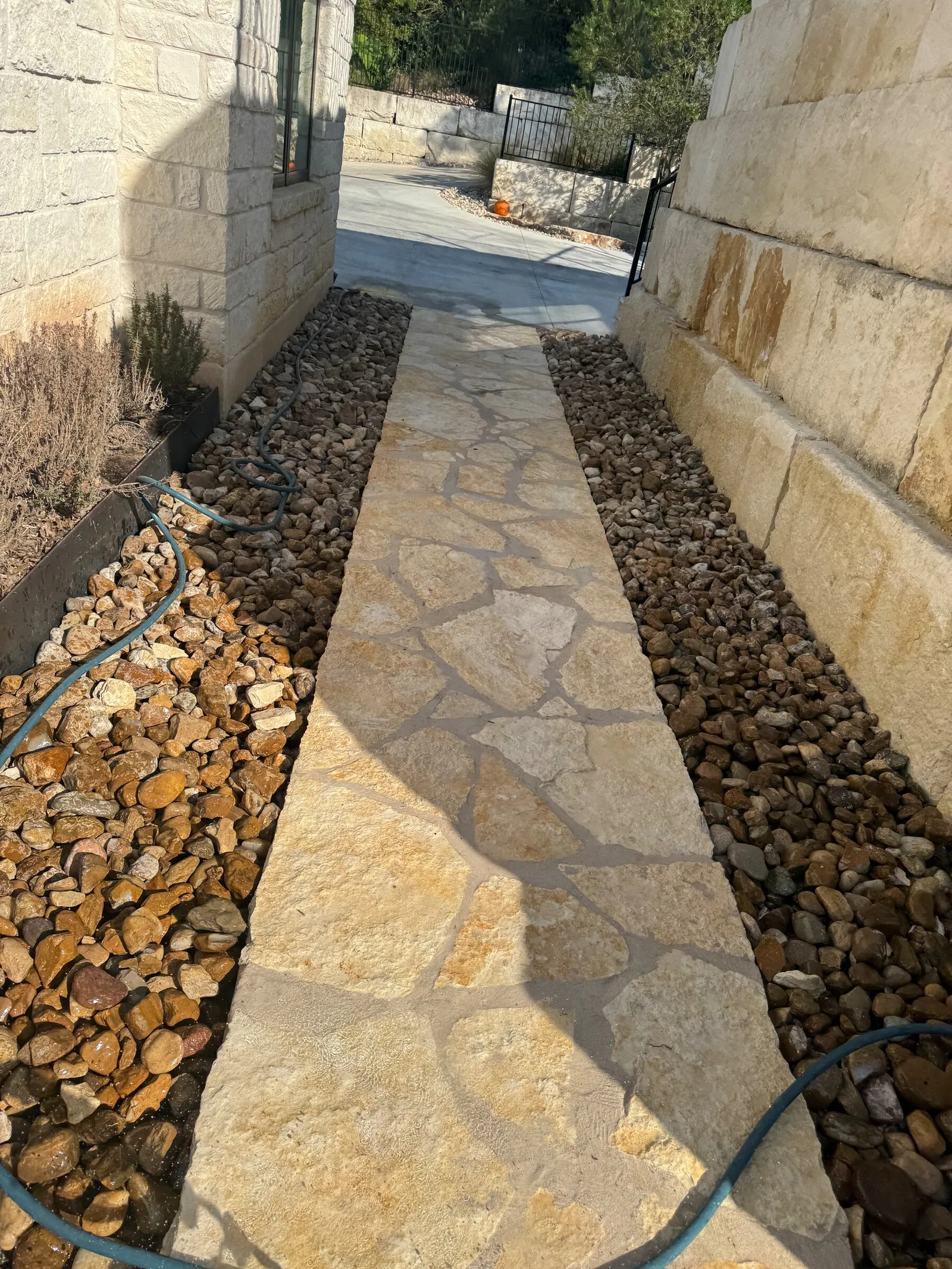 A fitted natural stone walkway between rock-covered beds beside a stone house.